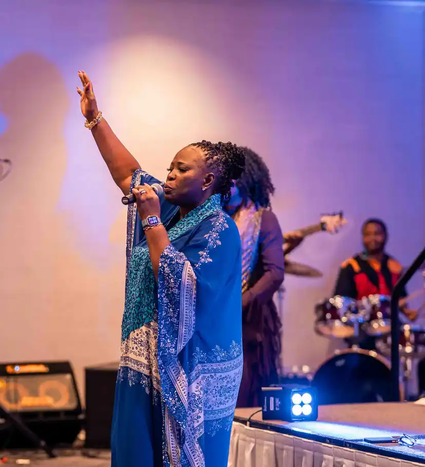 A worship leader singing with her arm raised, the band behind her